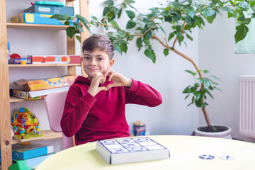 little boy playing tic-tac-toe. Boy shows heart gesture. Early child development topic, autism correction, child psychologist, speech therapist, psychiatrist