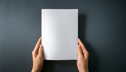 A pair of hands holding a piece of blank white A4 paper; grey background; graphic resources; graphic elements; top angle view of a pair of hands holding a blank white piece of paper; mock up photo