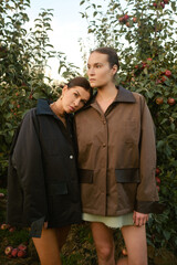 Two stylish girls in jackets at a fashion show in the apple orchard. Fashion show in the garden