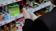 © Alexander - A customer in black studies the label on a bottle of sauce. Shopper carefully examines the ingredients and nutritional information on a bottle of sauce in a grocery store before buying