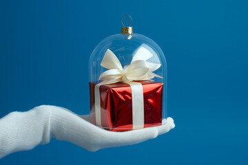 Hand holding a glass cloche with gift box inside, minimalist creative concept. Hello winter, Happy New Year, Merry Xmas, seasonal food, giftbox, Christmas sales, winter holidays mood in a cloche jar