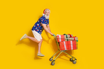 Full body portrait of stylish santa pushcart giftbox christmas print shirt isolated on yellow color background