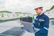 © ultramansk - A worker in protective gear uses a laptop while inspecting solar panels on a rooftop. The image emphasizes the use of technology in managing renewable energy systems and solar power installations.