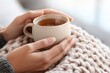© Сергей Захаров - Hands cradling hot cup on cozy knitted blanket