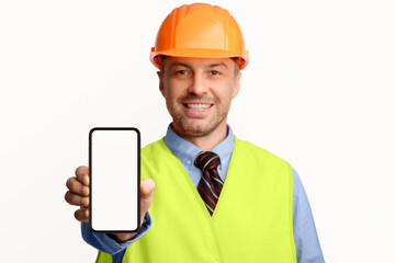 Poster - Building Services. Construction Worker Showing Cellphone Empty Screen Smiling To Camera Standing On White Studio Background. Selective Focus, Mockup