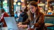 © thodonal - Young woman working on laptop in a busy café environment
