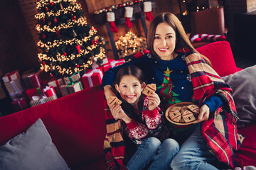 Wall Mural - Photo of two peaceful people mother daughter sit couch cuddle hold cookies new year xmas garland lights apartment indoors