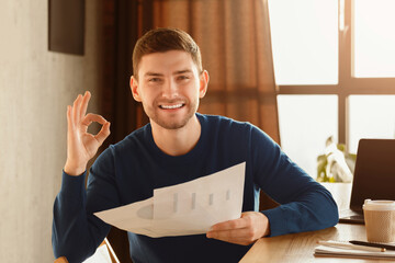 Poster - Business Startup Idea. Happy Guy Gesturing Okay Holding Papers With Graphs And Charts Sitting At Workplace Indoor. Selective Focus