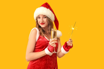 Wall Mural - Young woman in Santa Claus costume with glass of champagne and sparkler on yellow background