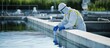 © Fana Art - A worker in a white protective suit and blue gloves takes a water sample at a water treatment plant.