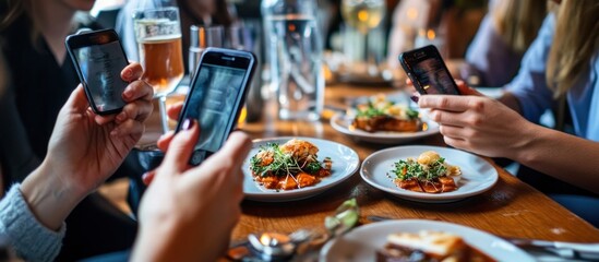 People using their smartphones at a restaurant table with food in front of them.