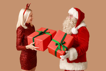 Santa Claus and beautiful mature woman in Christmas deer horns with gift boxes on brown background