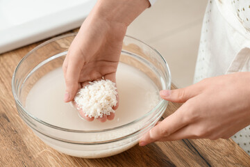 Woman rinsing rice in glass bowl near wooden table, closeup