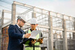 © SAHARAT - Two construction engineers are discussing about building construction plans at a construction site.