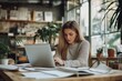 © StockUp - A woman engaged in work on her laptop in a well-lit, cozy modern office filled with plants and natural light.