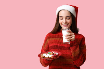 Wall Mural - Young woman with tasty Christmas gingerbread cookies and milk on pink background