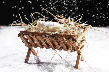 Manger with baby Jesus and hay on snow against dark background