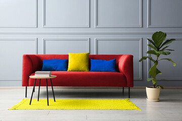 Wall Mural - Stylish red sofa with cushions, green plant and table in room