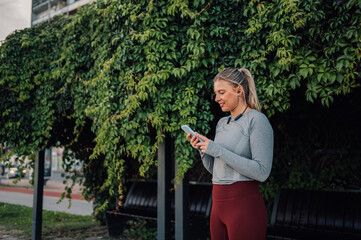 Wall Mural - Young sporty woman using smartphone outdoors after training session