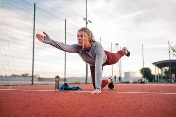 Wall Mural - Young sporty woman doing bird dog exercise at running track