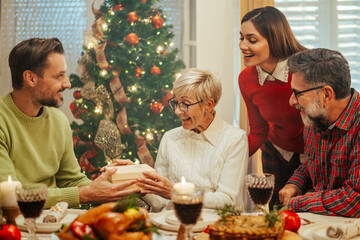 Wall Mural - Family giving christmas present to senior woman during christmas dinner