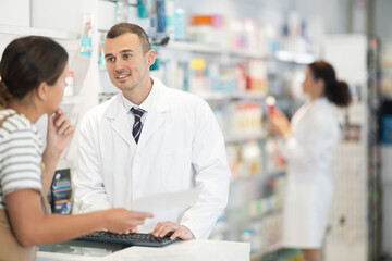 Wall Mural - Polite male pharmacist consulting young girl about medicine indicated in her recipe in chemist's shop