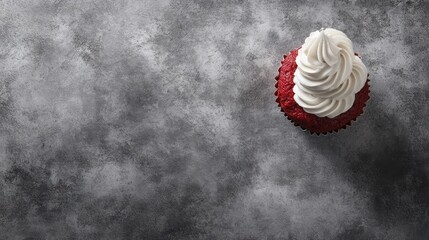 A single red velvet cupcake topped with swirls of white frosting on a textured gray background.