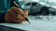 © Marketplace - A hand writing on a document with a pen, with a blurred car in the background, symbolizing insurance or automotive transactions.