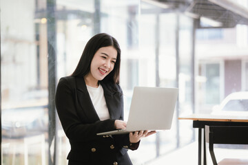 Beautiful Asian businesswoman talking on the phone using laptop in office