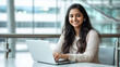 © colnihko - Confident Indian young professional woman working on laptop in modern office setting