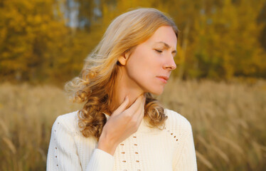 Sick exhausted woman suffering from acute sore in throat flu, touches neck with hand outdoor in park