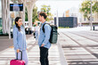 © Iryna - Two young adults, a man and a woman, meeting at modern outdoor transportation hub. Woman holds pink suitcase, while man carries backpack. Bright sunny day enhances atmosphere of travel