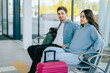 © Iryna - Young Caucasian couple seated in airport terminal awaiting flight. Man and woman dressed casually with luggage, modern travel environment Excitement and anticipation.