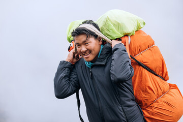 portrait of strong sherpa man working as porter carrying a huge cargo with traditional method on for