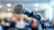 © Yuan - A microphone on a stand in front of a blurred audience.  The microphone is ready for a speaker to address the crowd.