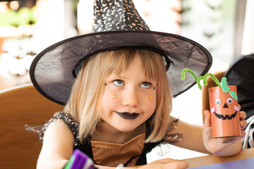 Wall Mural - A cute girl in a witch costume makes a funny paper craft for Halloween. Children's crafts for Halloween.