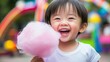 © Suphawan - Close-up of a young child taking a bite of pink cotton candy, with a joyful expression and colorful rides in the background. --chaos