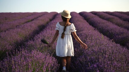 Wall Mural - Girl is walking through a field of purple flowers. She is wearing a white shirt and a hat.