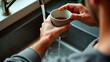 © Eva - A man's hand holds a cup and washes it in the sink of his modern kitchen, close-up view from above. The focus is on the hands. No faces should be visible. A cozy home atmosphere.