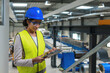 © 24K-Production - Indian woman in a blue helmet and yellow vest, worker in an industrial unit checking a work process, portrait. Industry, people, and career concepts.