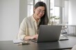 © ColorfulFlowerStudio - Smiling Asian Woman Working on Laptop at Home Office