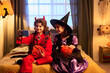 © pressmaster - Two happy little kids in Halloween costumes sitting on bed in domestic room and looking at smartphone screen during selfie