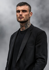 Tattooed male model with short hair standing in black t-shirt and blazer surrounded by mist exuding bad boy vibes