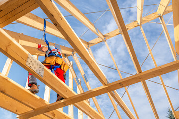 Construction Worker Securing Roof Beams at a Building Site Under a Clear Blue Sky