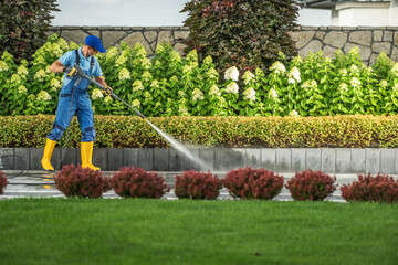 Wall Mural - Gardener Using a Pressure Washer to Clean Pathways in a Vibrant Landscaped Area on a Sunny Day