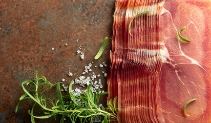 Sticker - Sliced prosciutto and rosemary on a brown rusty background.