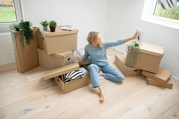 pretty, middle-aged blonde woman sitting on the floor of her new apartment, loft, house unpacking moving boxes