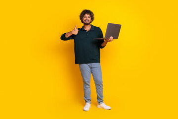 Cheerful man holding laptop against vibrant yellow background, wear casual attire, giving a thumbs up, representing online shopping