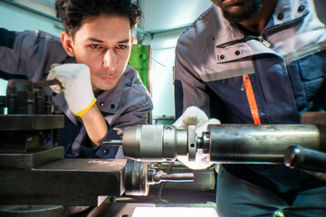 Two focused industrial technicians work together operating heavy machinery in a workshop. The image of teamwork, precision, and technical expertise in an engineering and manufacturing industry