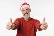© InsideCreativeHouse - Happy mature middle-aged man wearing Christmas Santa Claus red hat showing thumbs up looking at camera isolated in white background. New Year Merry Christmas winter holidays concept